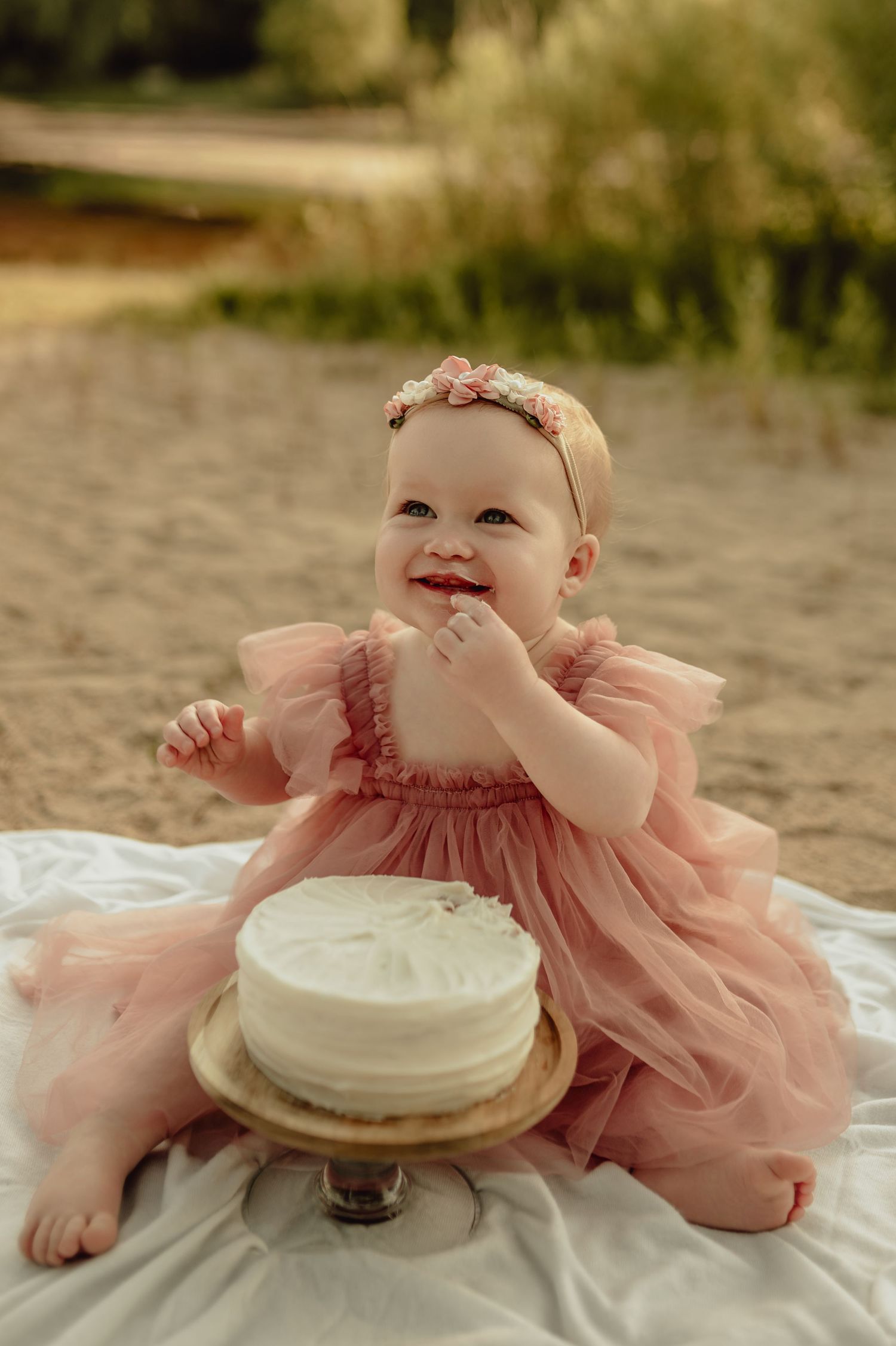 Baby in pink tulle dress having a cake smash photo session on white blanket.