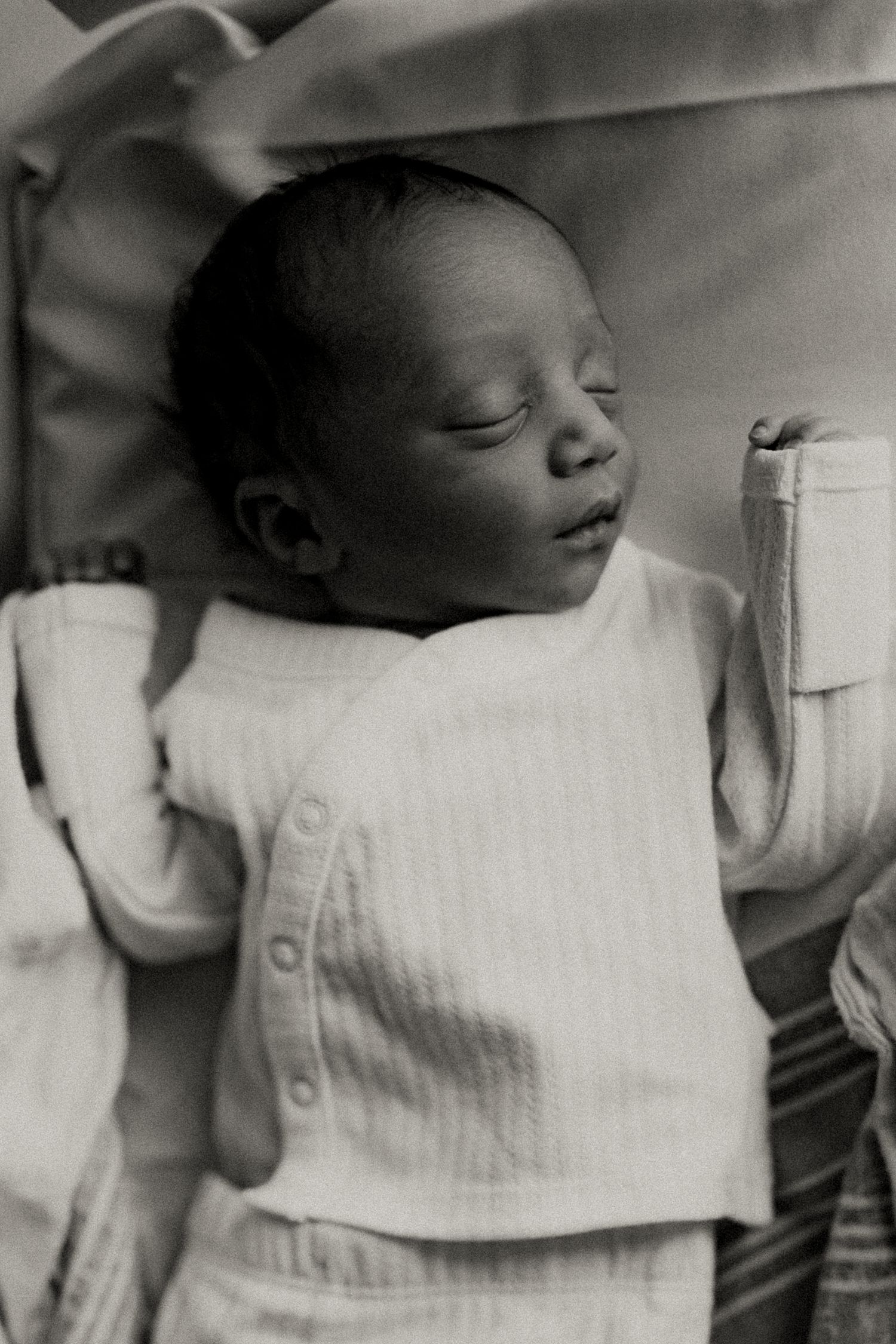 Peaceful sleeping newborn baby wearing white clothing rests in hospital bassinet.