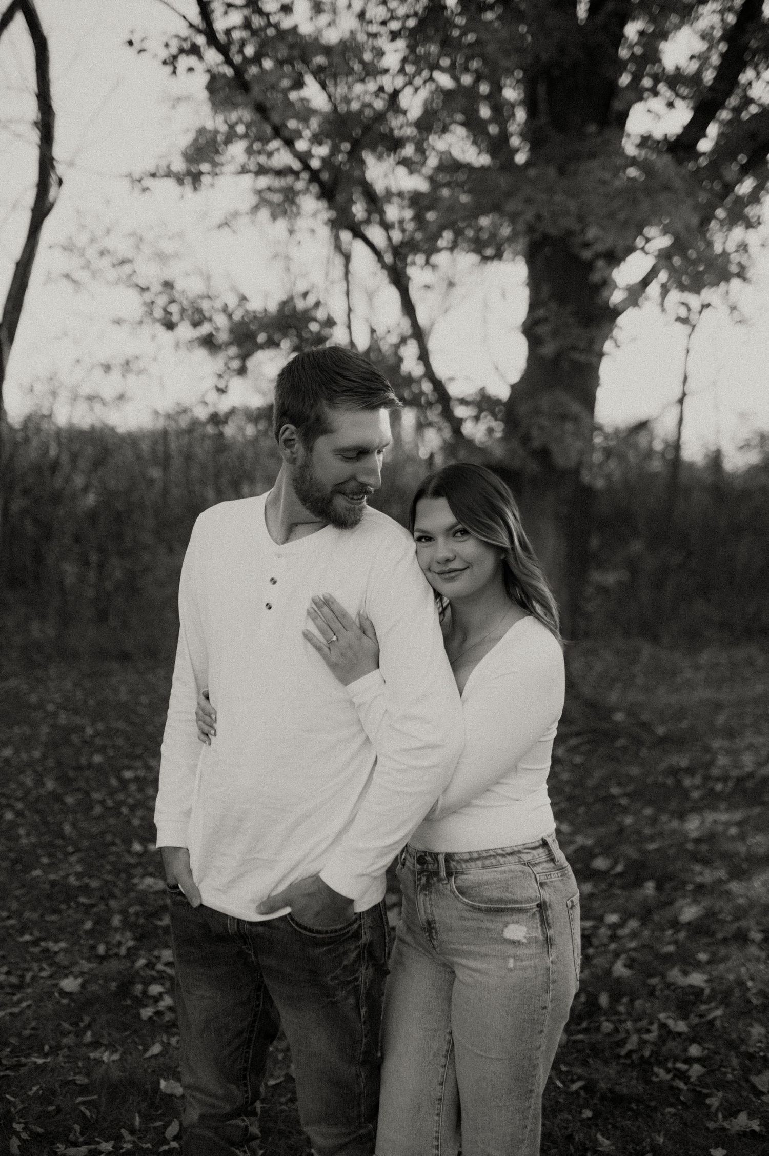 Black and white portrait of a couple embracing outdoors among trees.