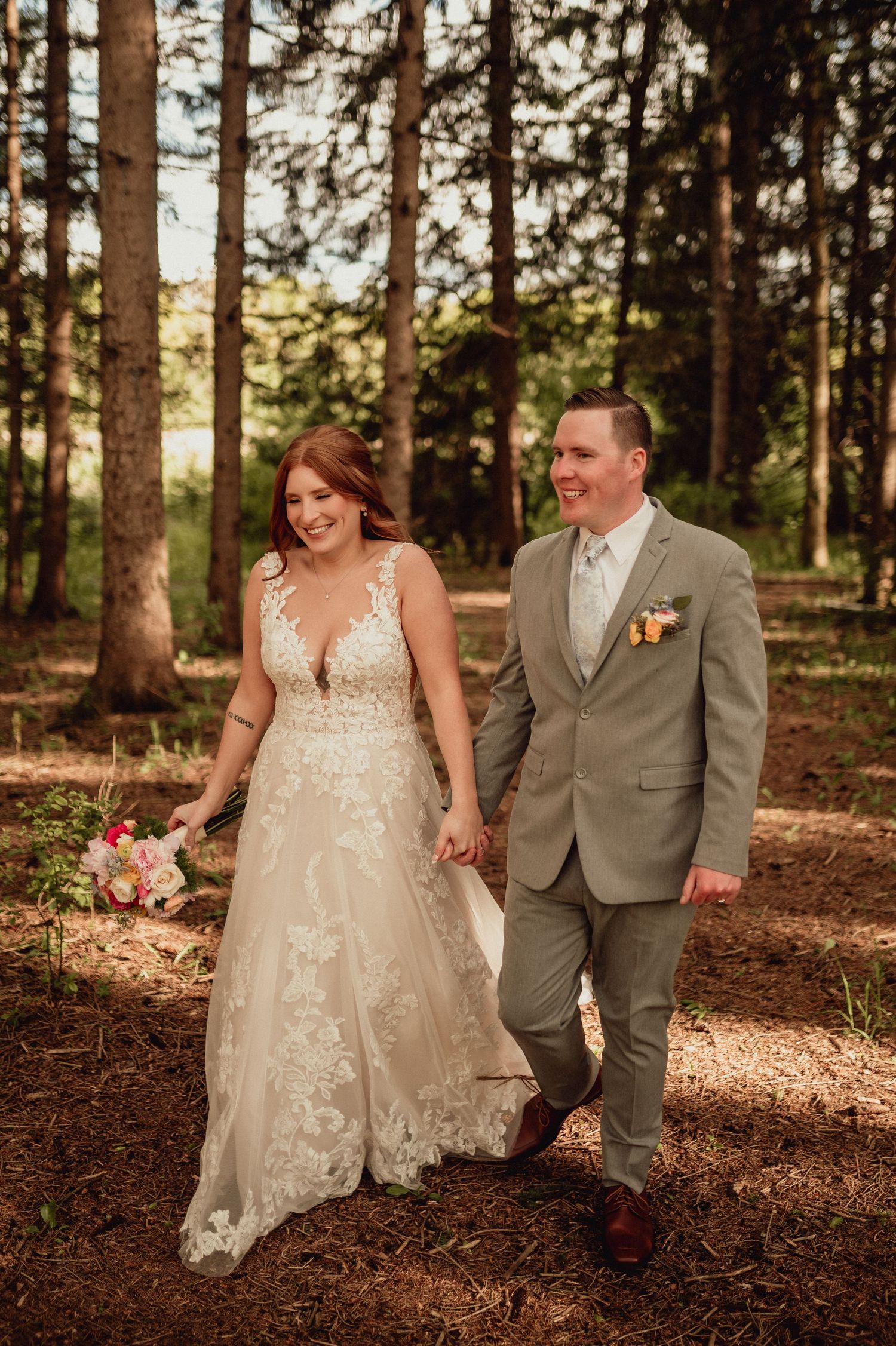A couple in wedding attire walks together through a sunlit forest during their autumn wedding photoshoot.