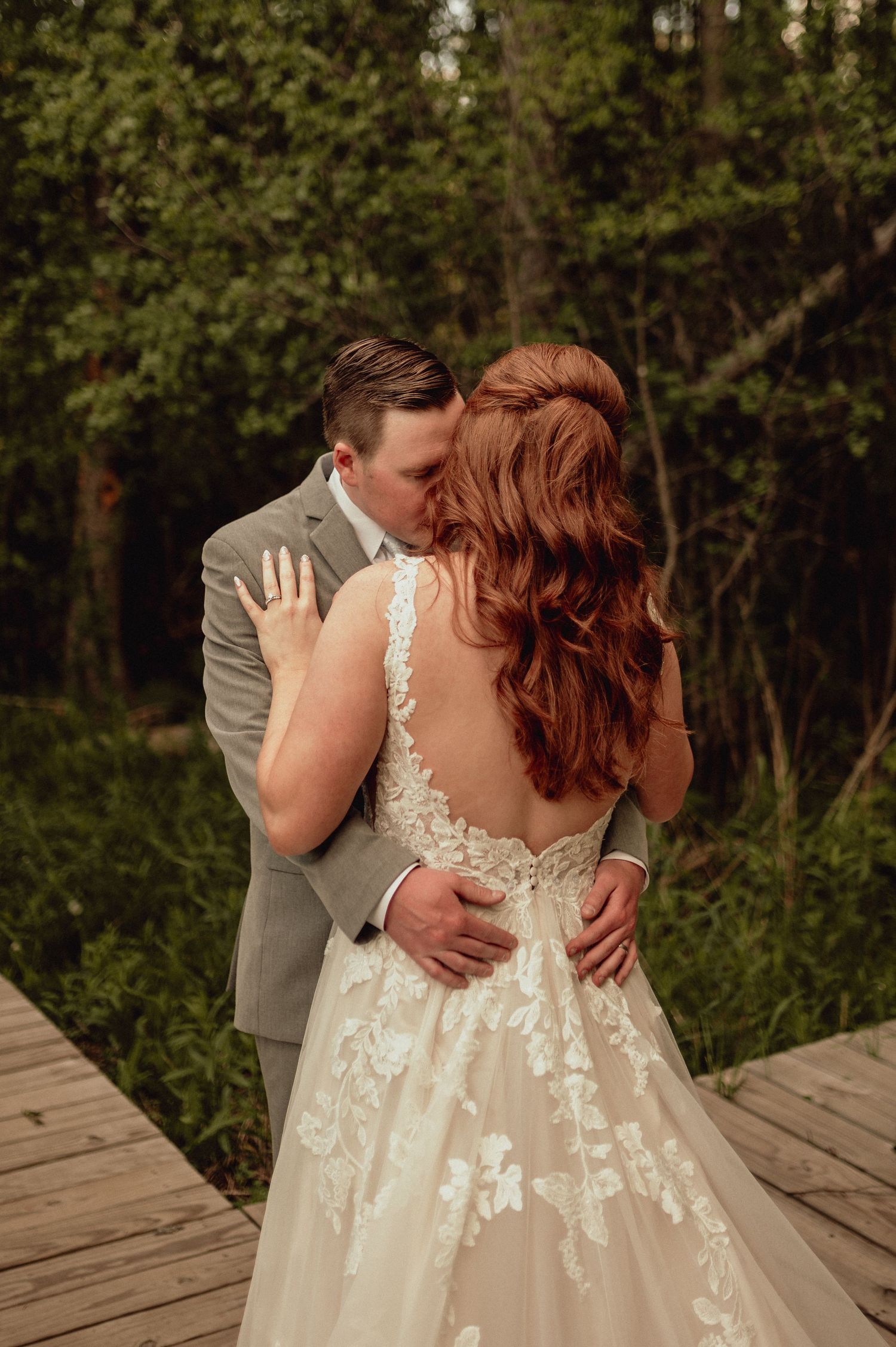 A romantic wedding couple embraces on a wooden deck surrounded by lush green forest during an intimate outdoor moment.
