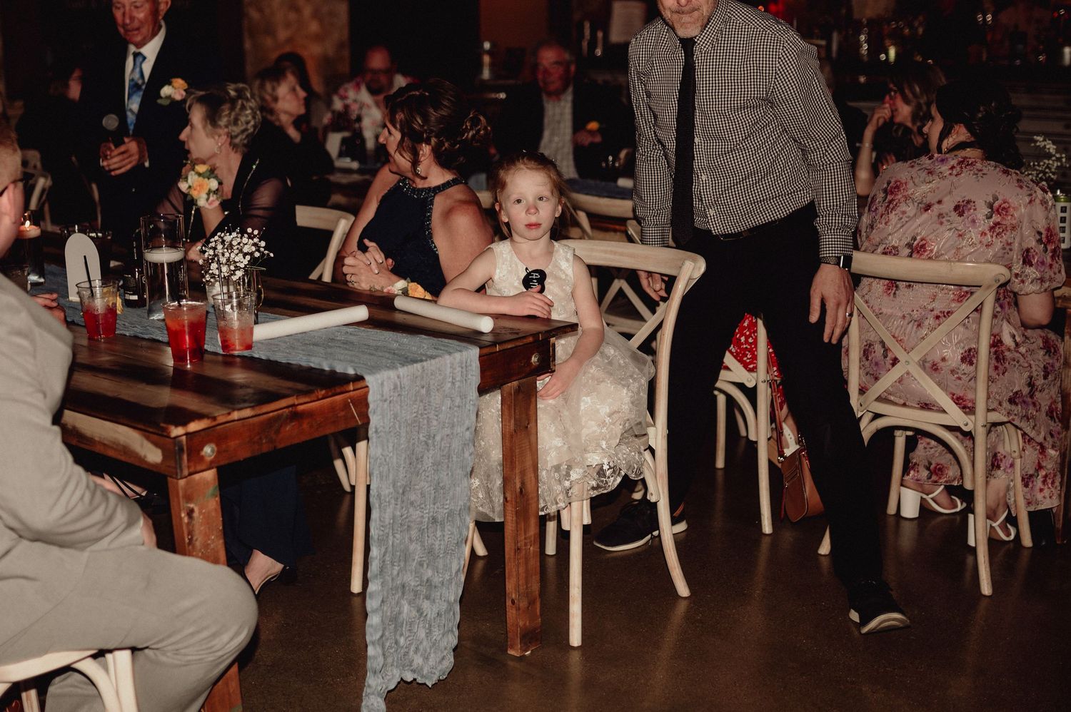 A lively crowd gathers at a retro-style bar with checkered tablecloths and wooden decor in a dimly lit setting.