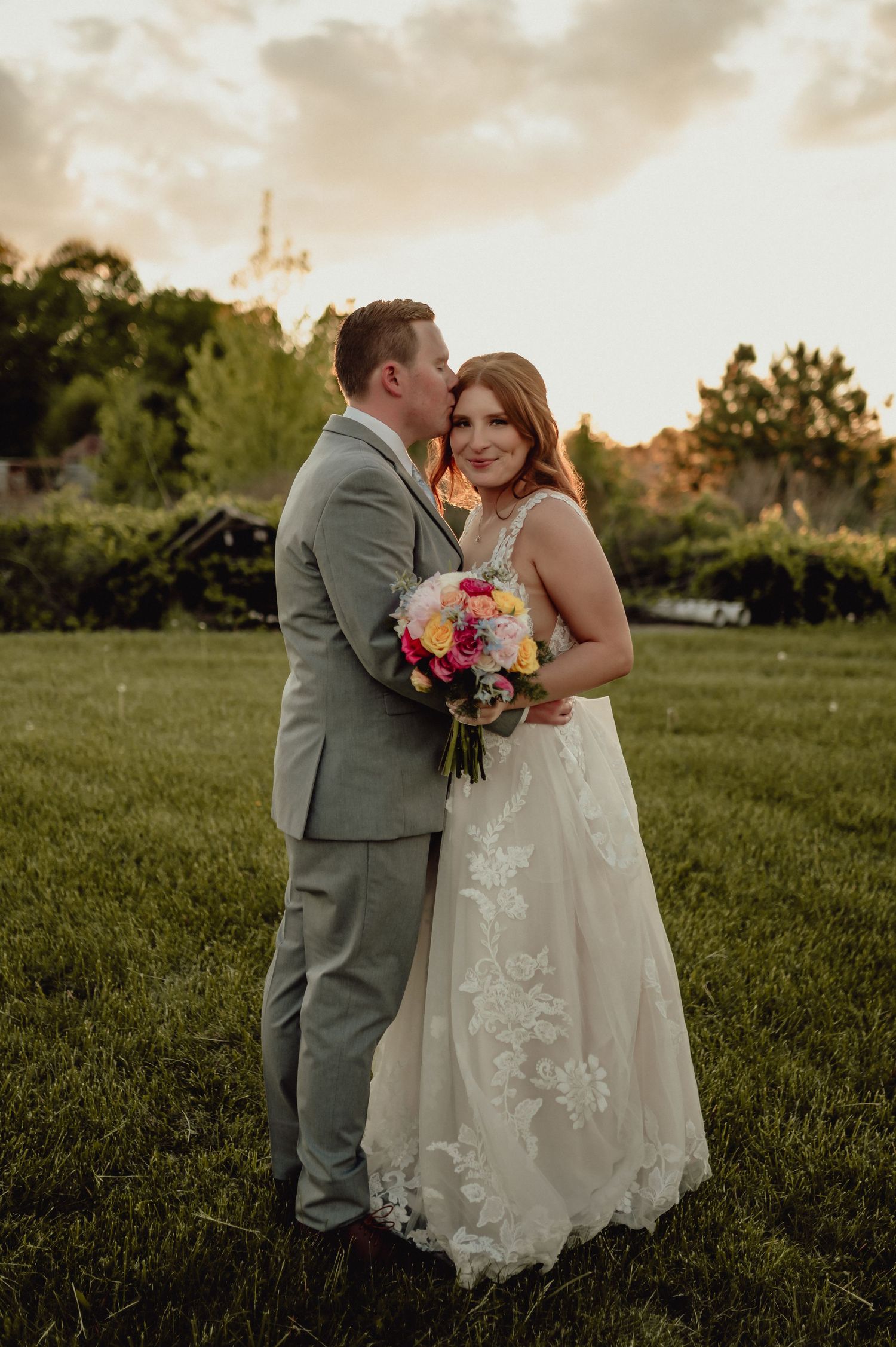 A couple embraces during their wedding photoshoot in a sunlit meadow.
