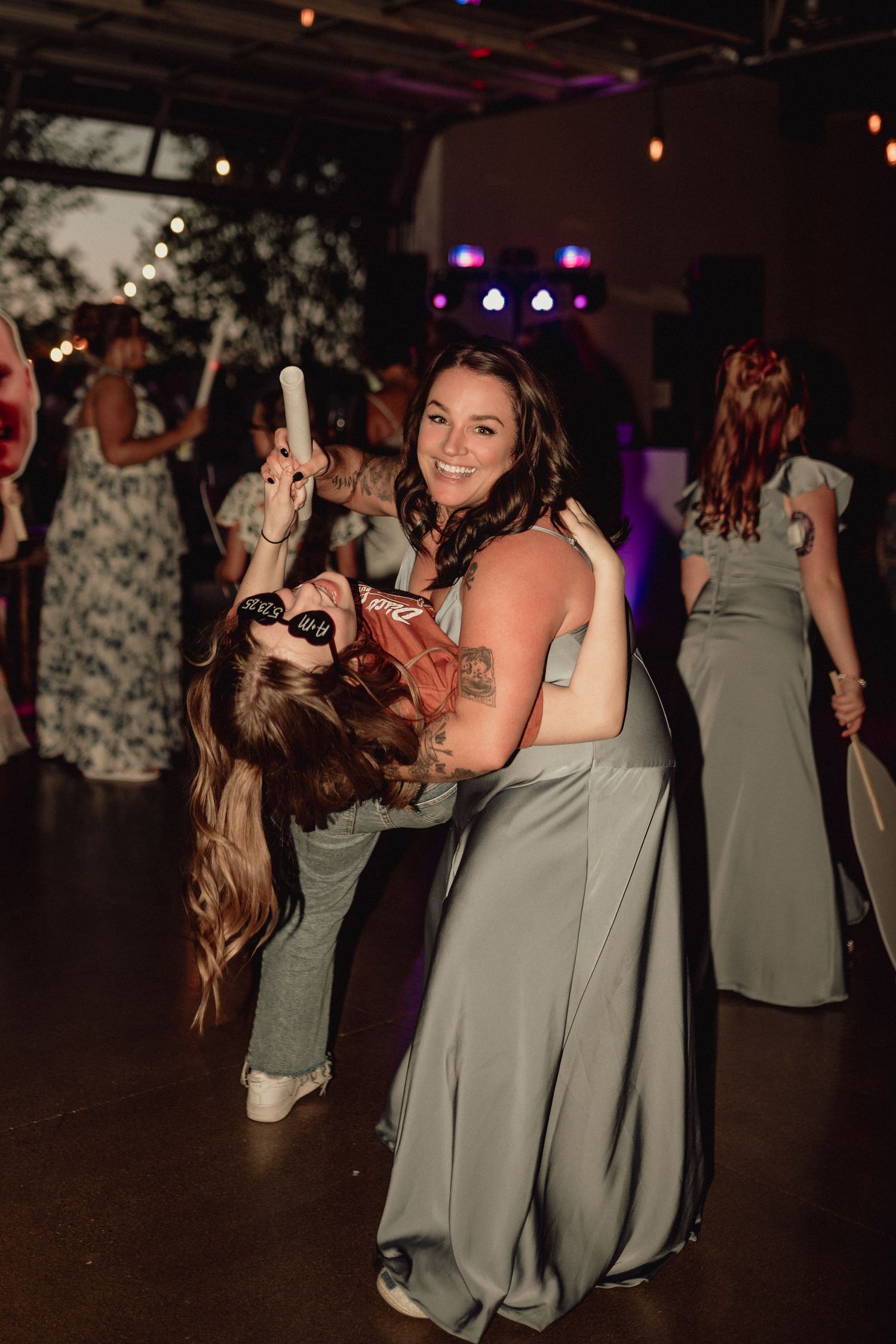Wedding guests in sage green dresses dance and celebrate together on a dimly lit dance floor.