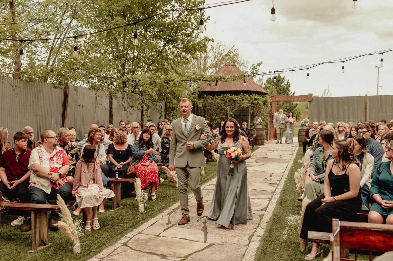 Outdoor wedding reception with string lights and guests mingling on a patio during golden hour.