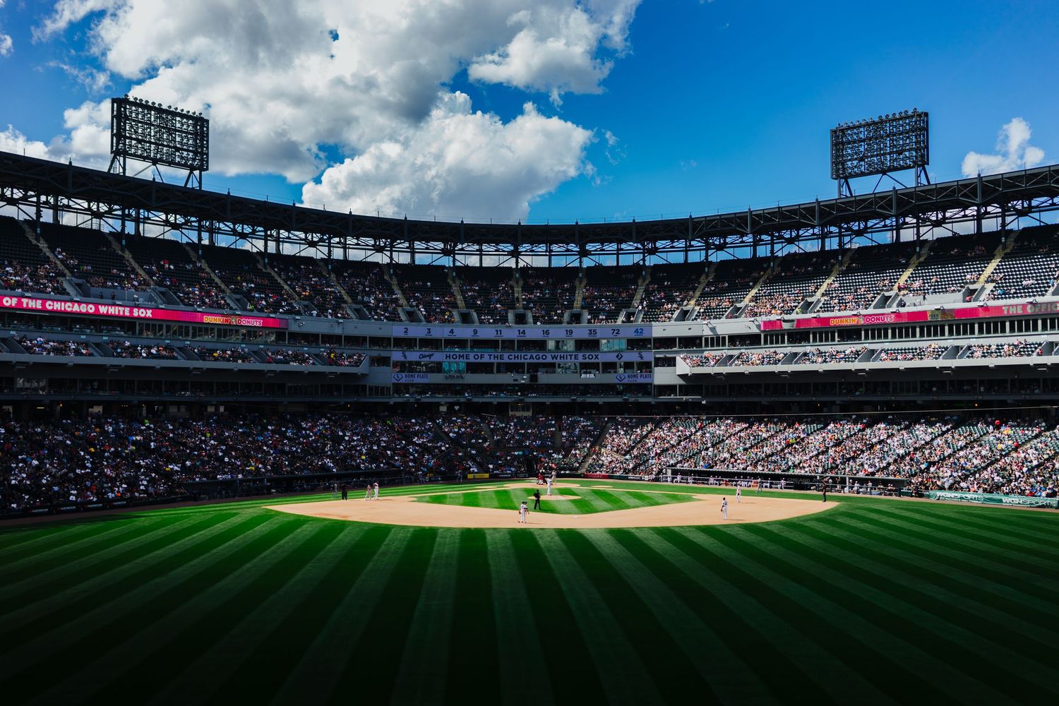 Panoramic view of a baseball stadium with bright blue sky and white puffy clouds overhead.