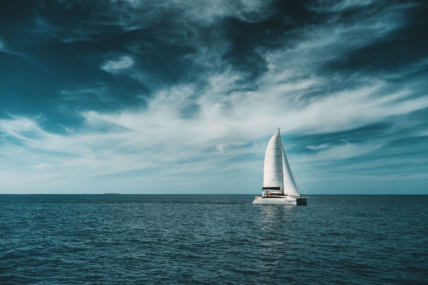 A dramatic stormy seascape with dark turquoise water and moody clouds reflected on the ocean surface.