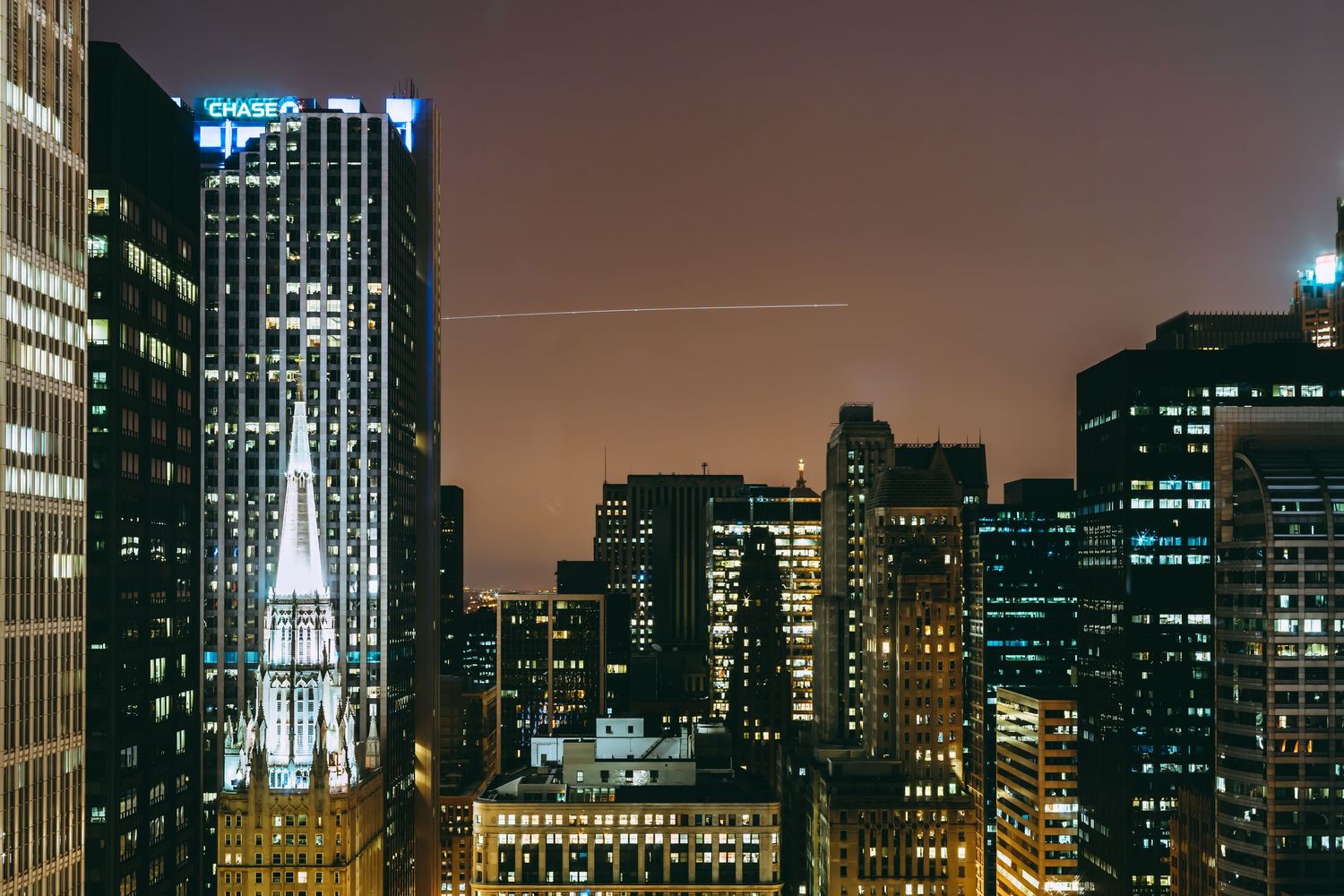 Illuminated city skyline at night with tall skyscrapers and glowing office buildings.