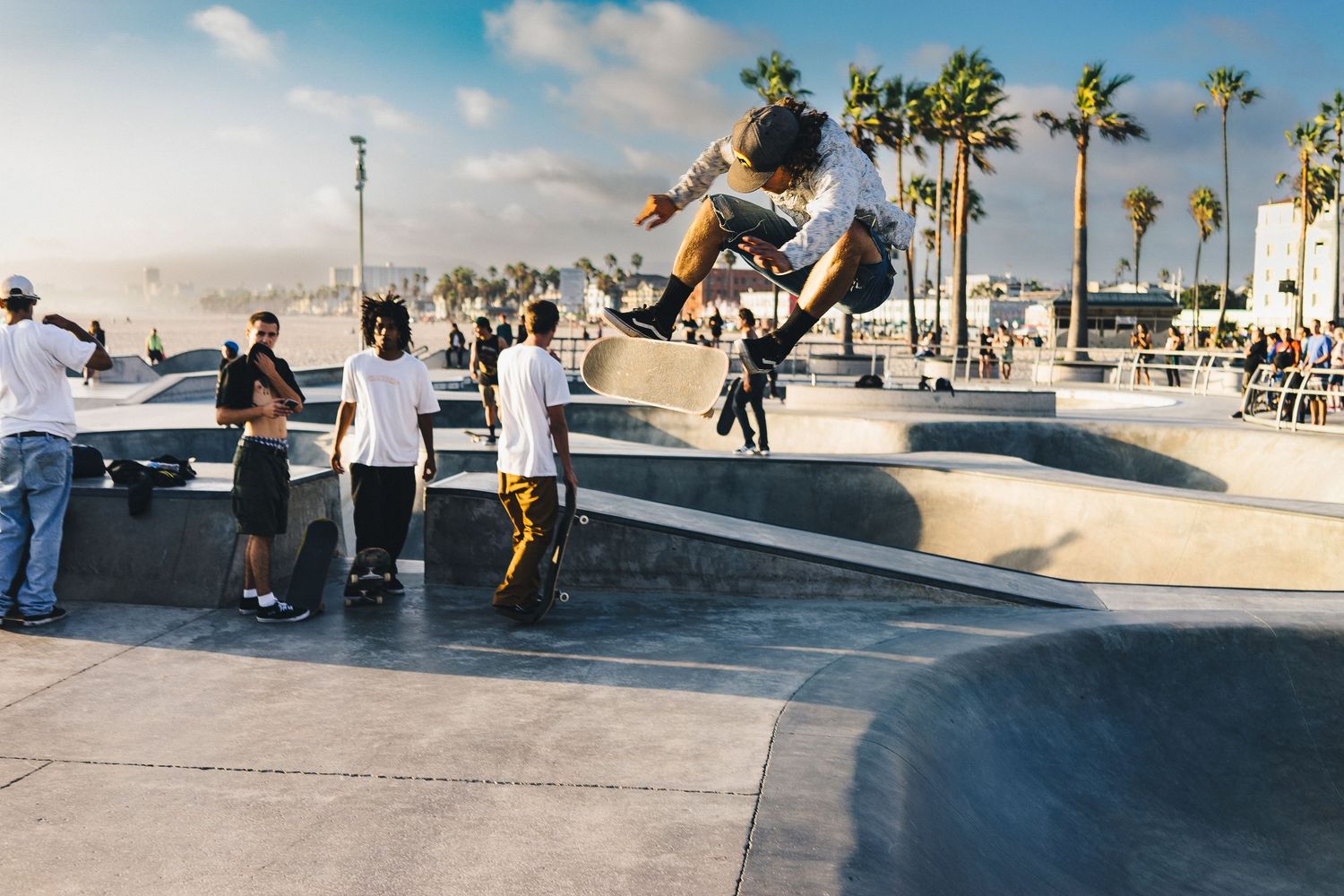 Skateboarders perform tricks at a beachfront skate park on a sunny day.