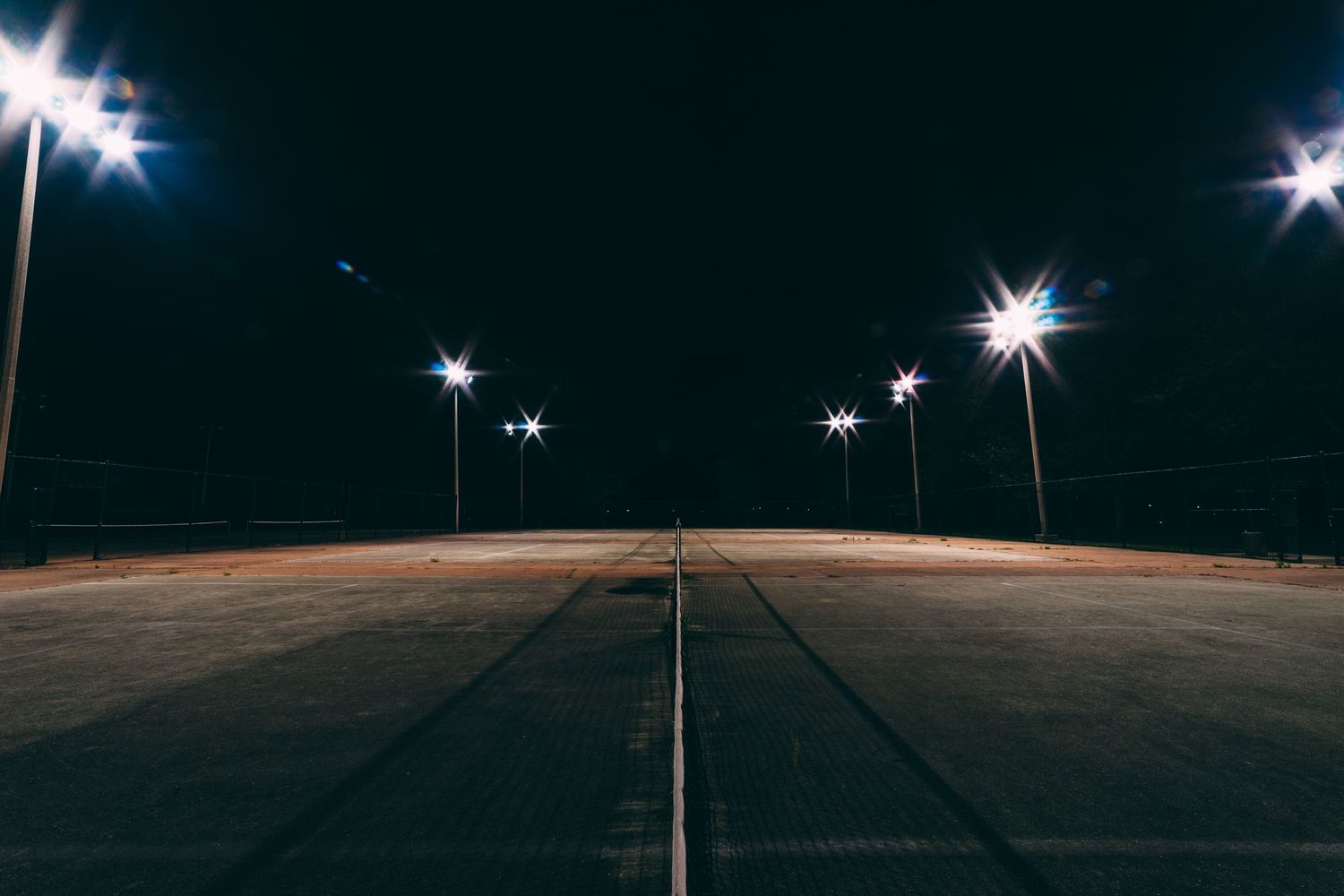 Street lamps illuminate a dark empty parking lot at night.