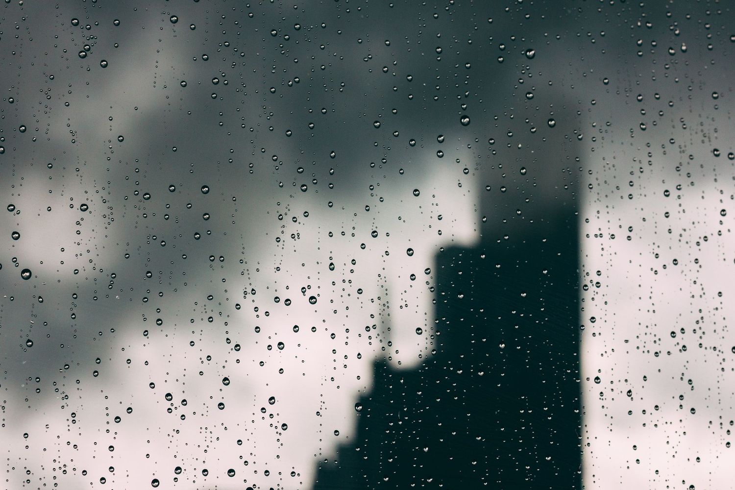 Raindrops on a glass window creating a blurry abstract pattern against a dark background.