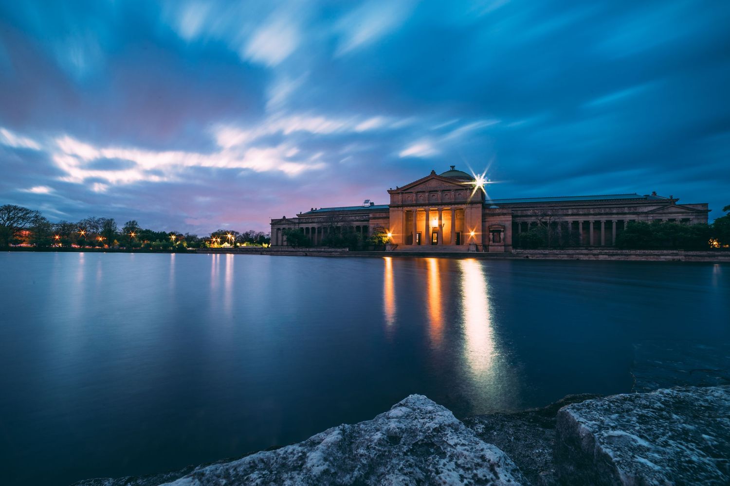 Serene coastal panorama at twilight with illuminated buildings reflecting on calm waters.