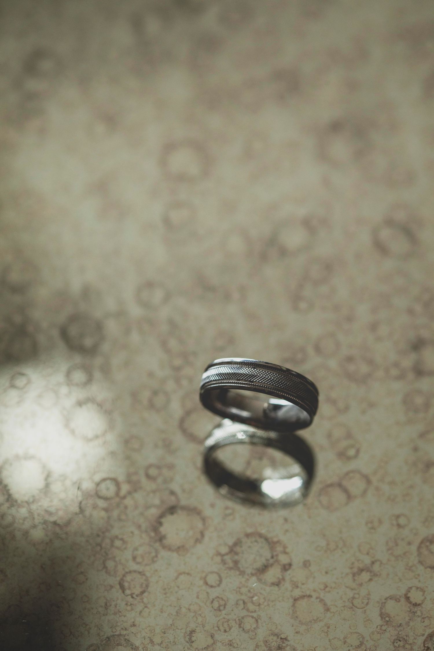 Close-up sequence of a silver wedding ring on textured beige surface.