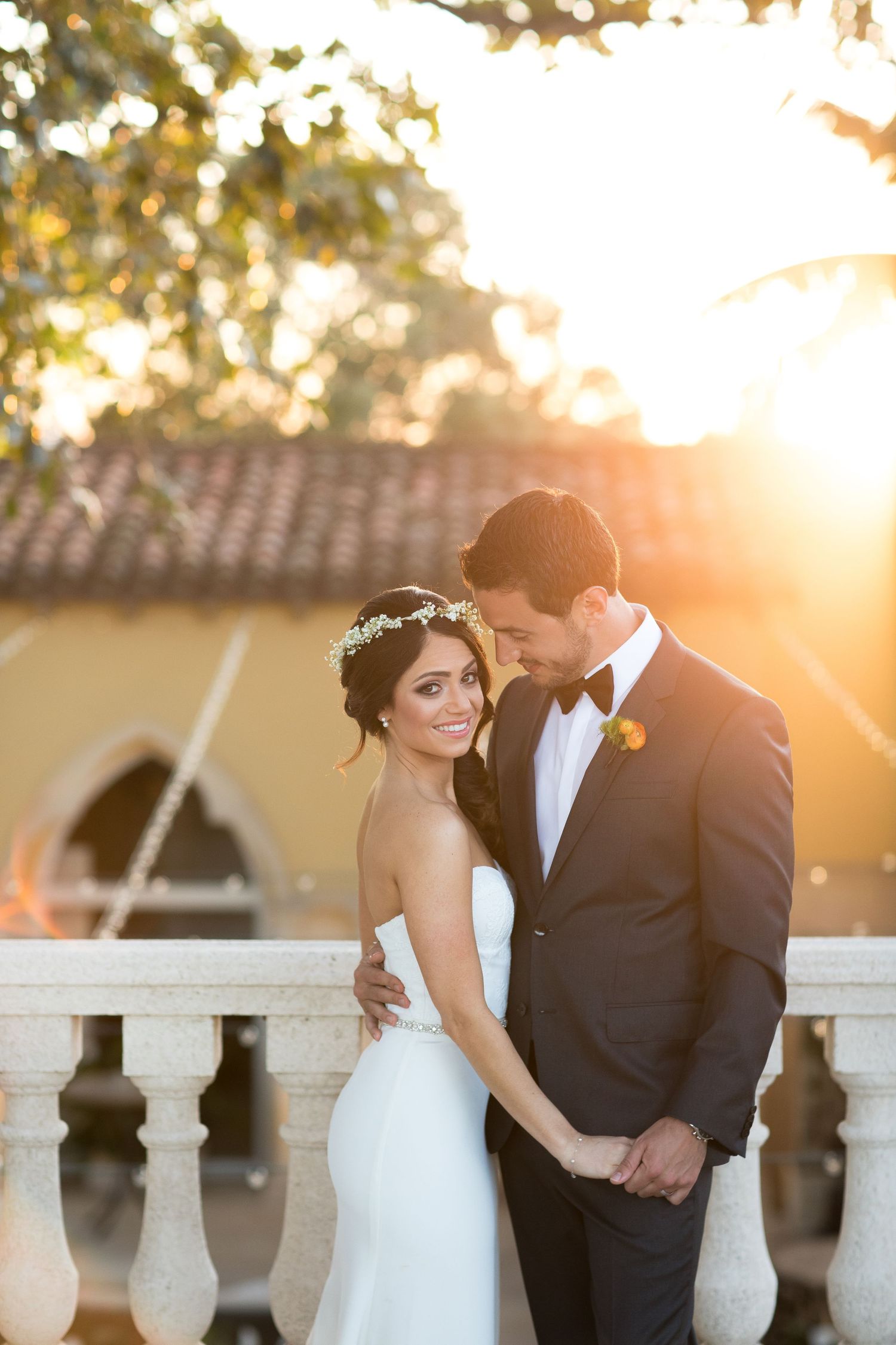 Wedding couple poses against a sunset backdrop with Mediterranean architecture.
