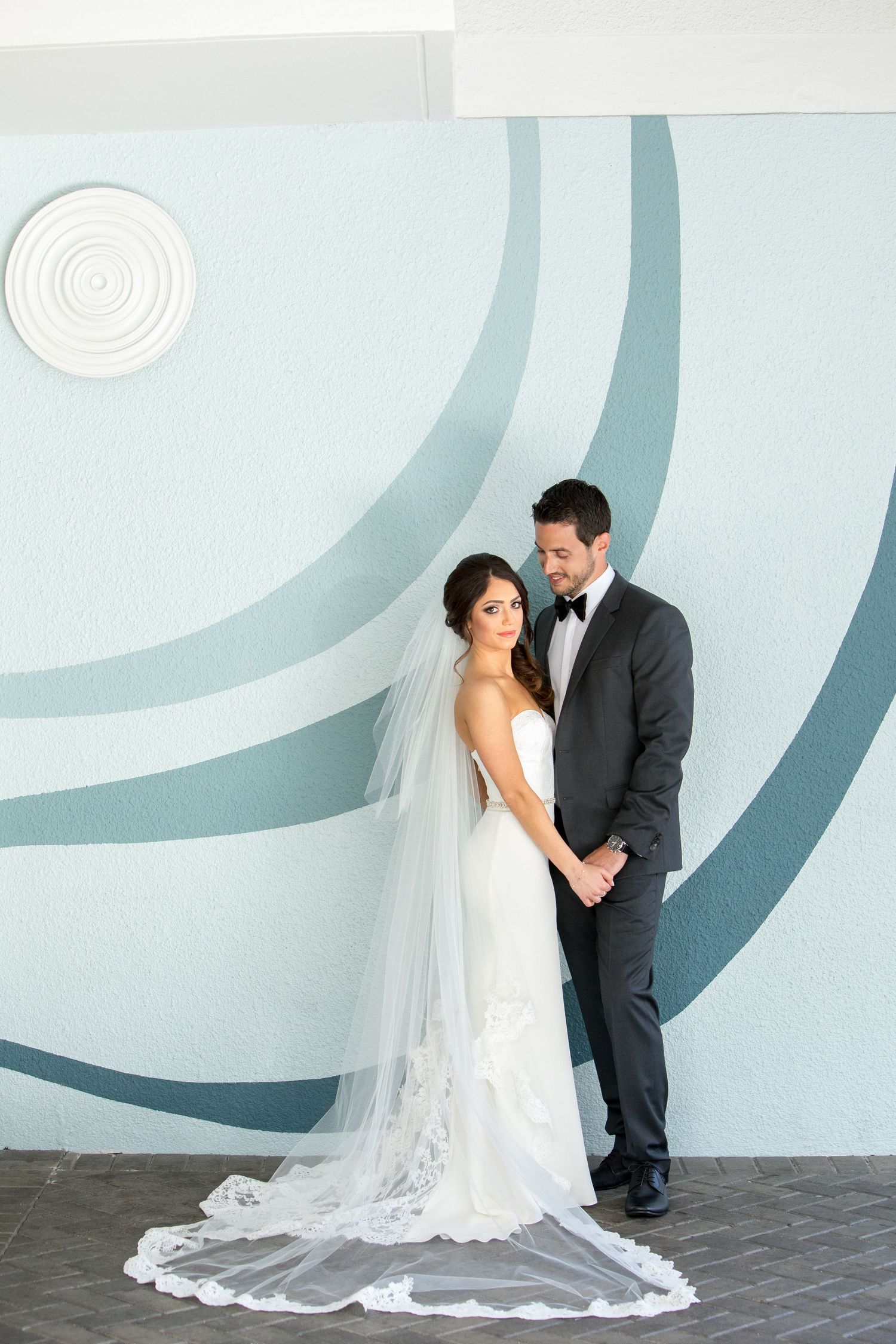 Elegant wedding portrait against modern blue geometric wall with flowing veil.
