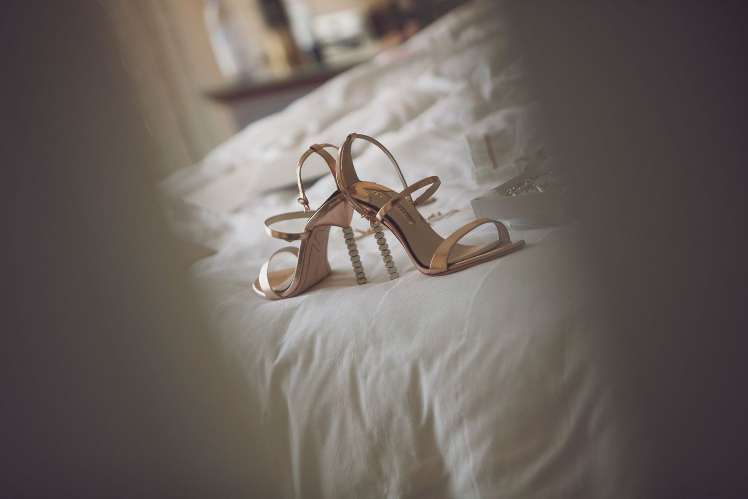 Elegant bridal sandals resting on white bedding in soft focus.