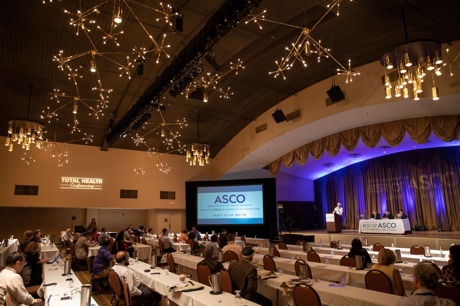 Elegant ballroom setup with round dining tables and sparkling chandeliers illuminating the dimly lit event space.