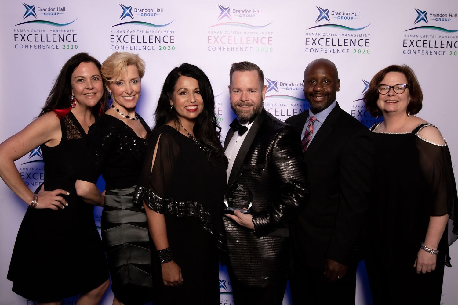 Group of people in formal attire posing together at an Excellence award ceremony event.