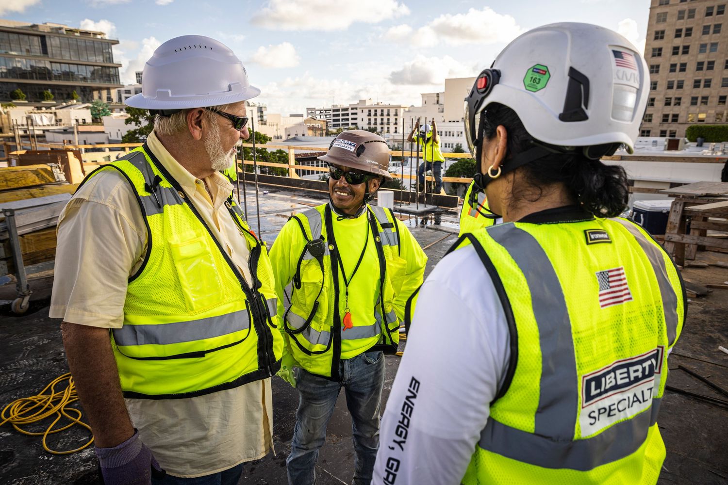 Construction workers in yellow safety vests and hard hats inspect a building project site.