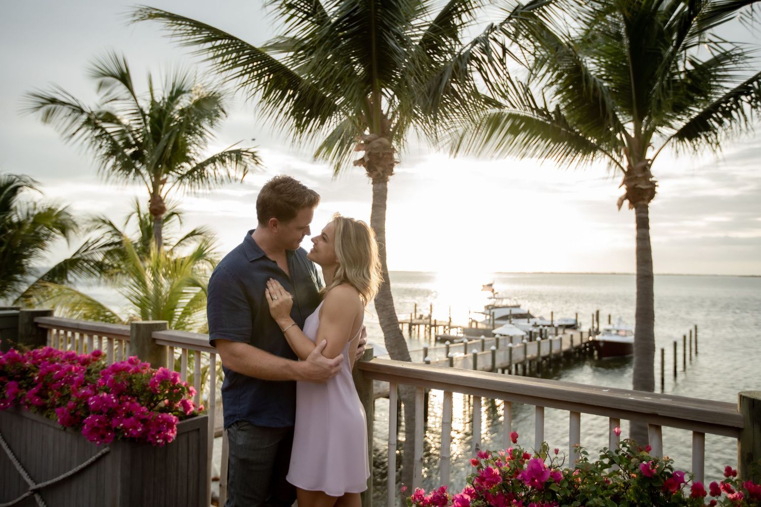 A romantic beach scene with palm trees and vibrant bougainvillea flowers in the foreground.