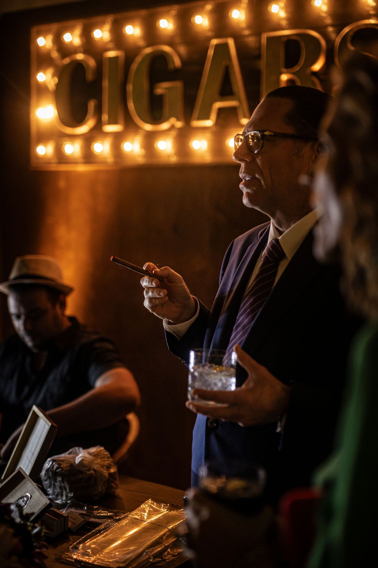 A dimly lit bar with illuminated CIGARS sign displaying drinks and tobacco accessories in an upscale environment.