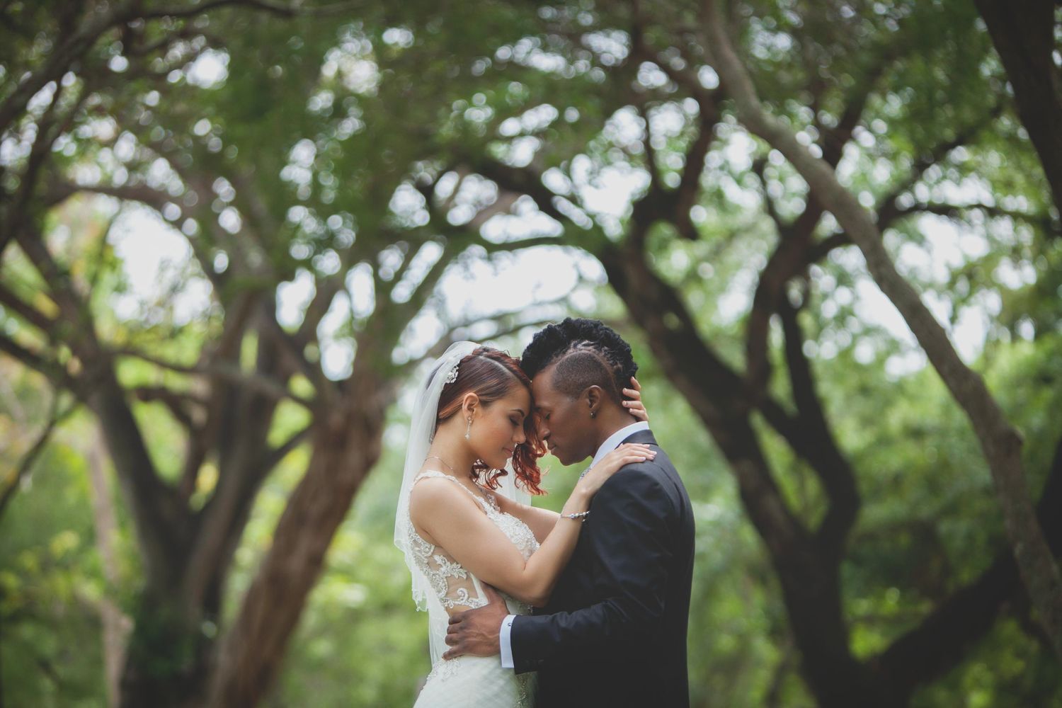 Romantic outdoor wedding moment captured under lush green trees.