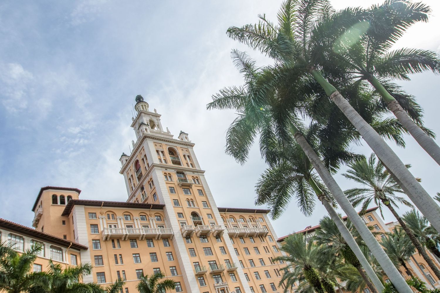 Historic beige building with Spanish colonial architecture features tall palm trees and elegant design details.