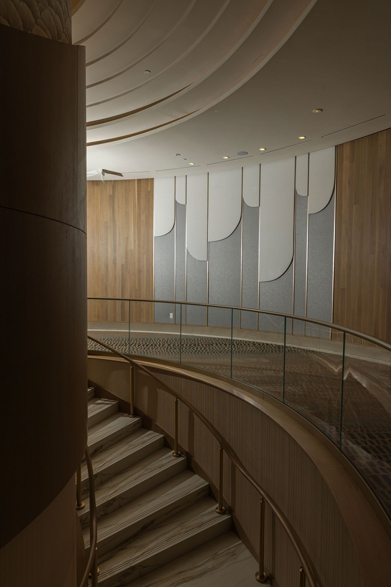 Modern interior staircase with curved glass balustrade and wooden panels illuminated by soft lighting.