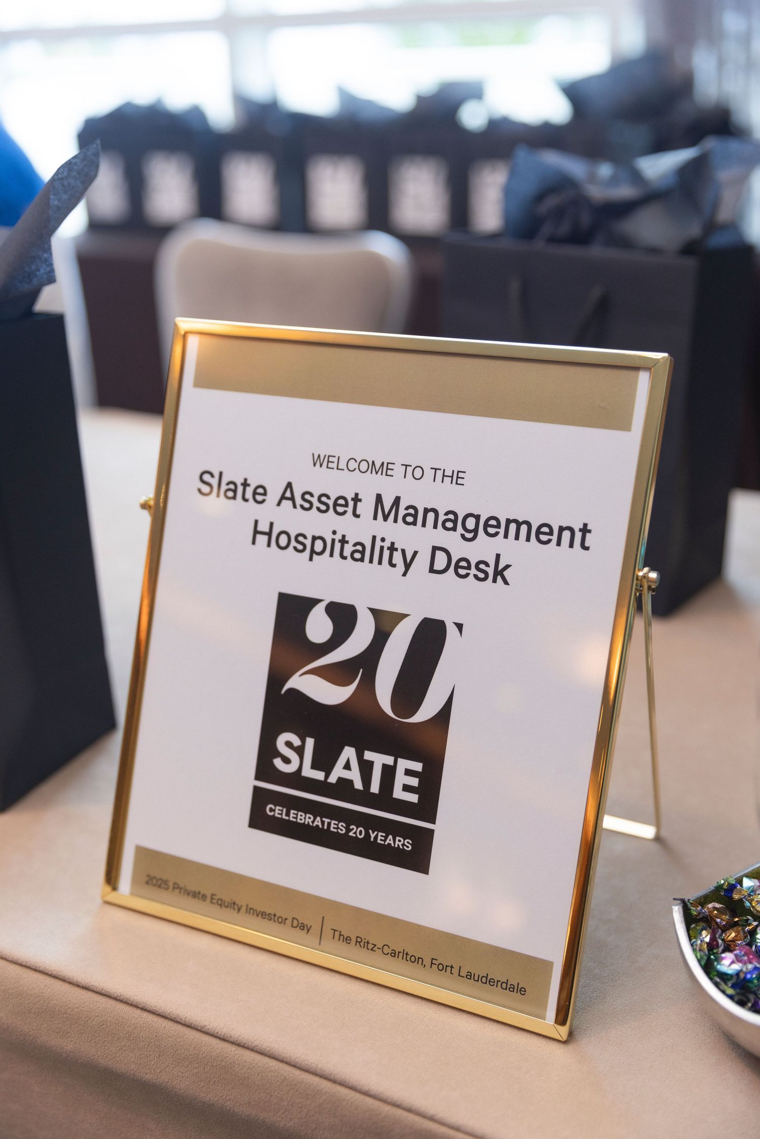 Gold-framed welcome sign for Slate Asset Management Hospitality Desk with 20th anniversary logo display.