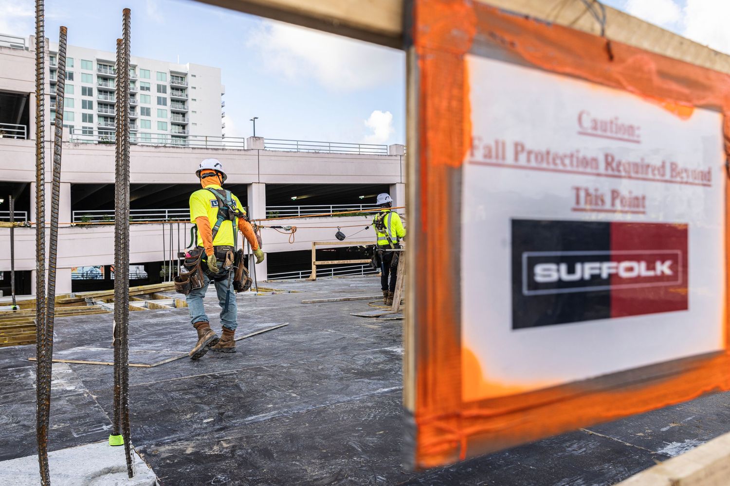 Construction workers install fall protection safety barriers along the edge of a commercial building rooftop.