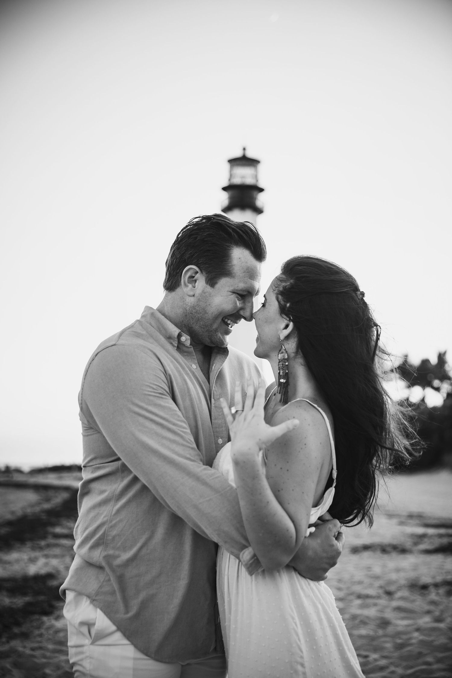 Romantic beach photoshoot with a lighthouse in background at sunset.