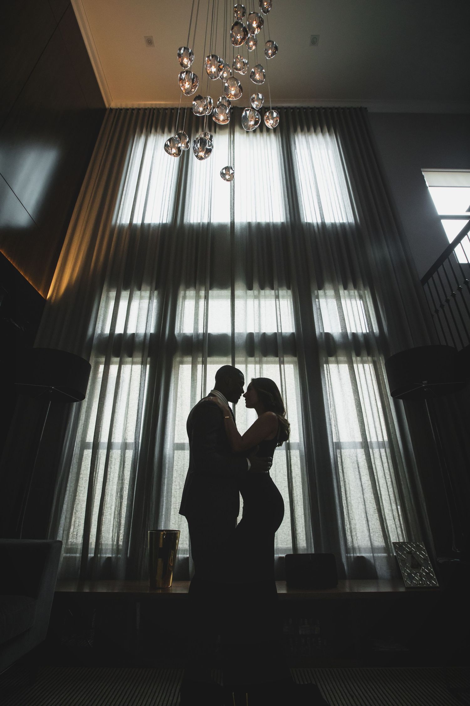 Silhouetted figures against bright window with crystal chandelier in foreground.