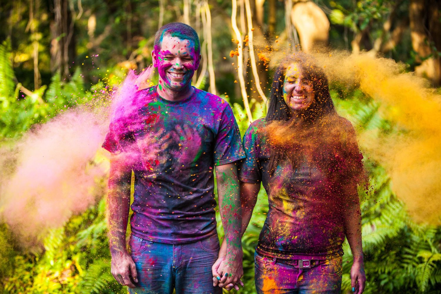 Joyful couple covered in colorful holi powder during outdoor photo session.