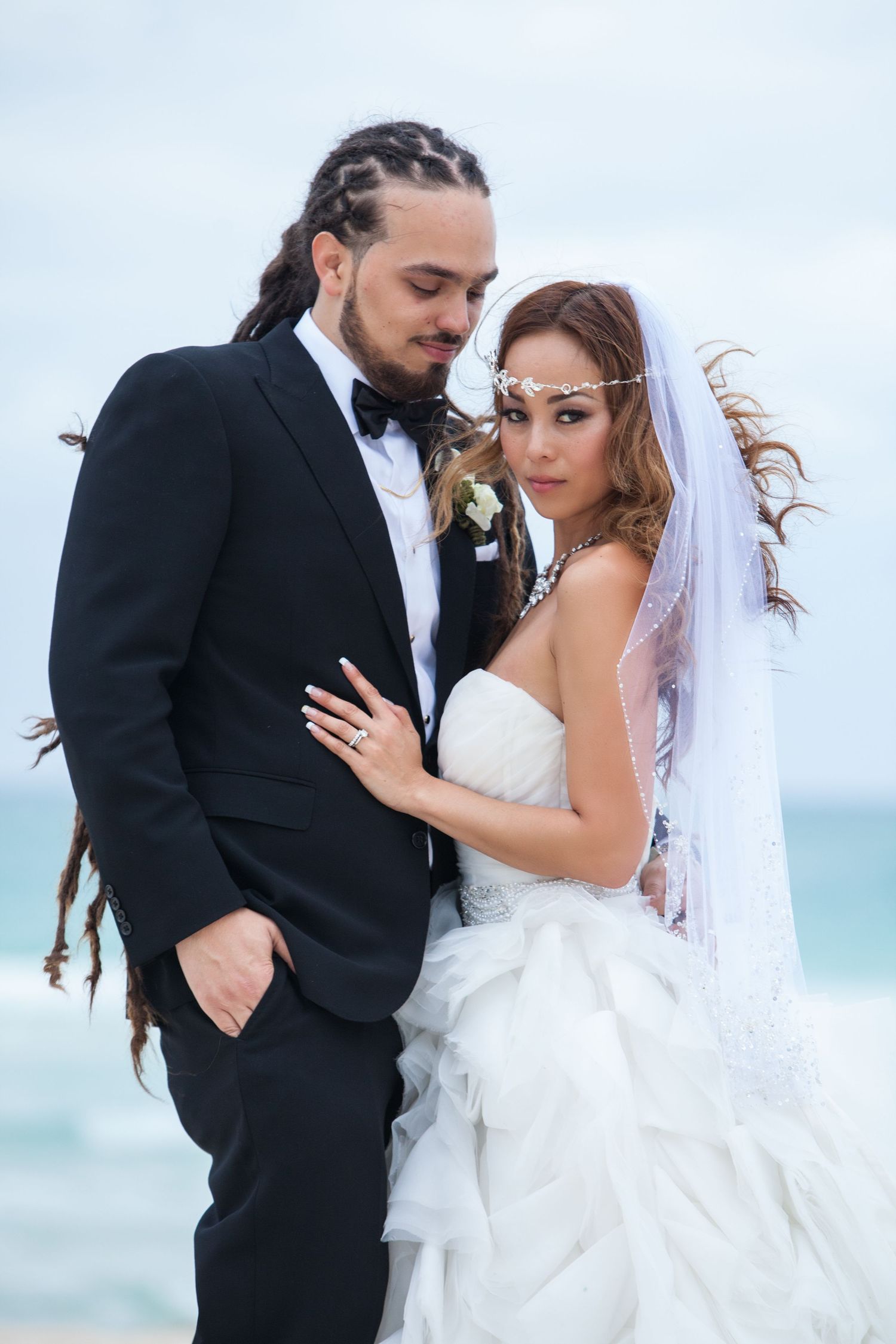 Newlyweds share an intimate moment on a windy beach with white wedding dress flowing.