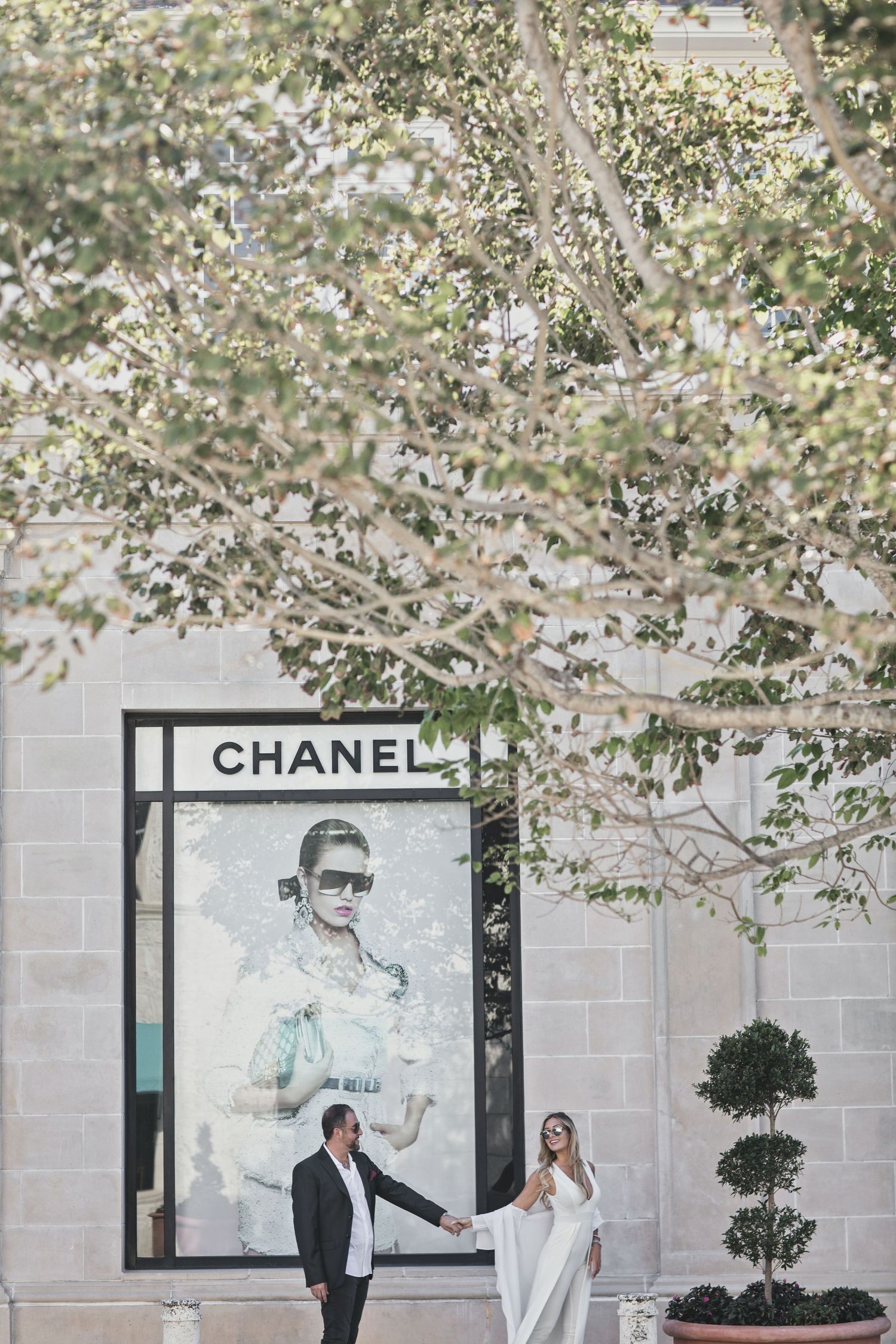 Romantic spring engagement photos under blooming cherry blossom trees near Chanel store.