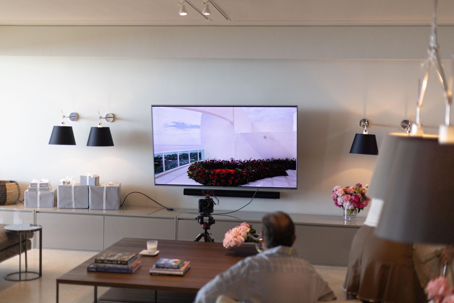 Modern living room with large flat-screen TV, camera on tripod, and elegant furniture in a minimalist setting.