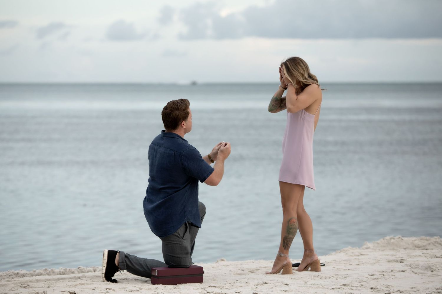 Silhouettes on a beach as someone kneels in a proposal pose at sunset.