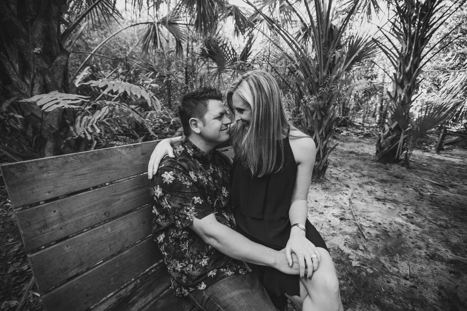 Two people embracing in a romantic kiss amidst a lush tropical garden setting.