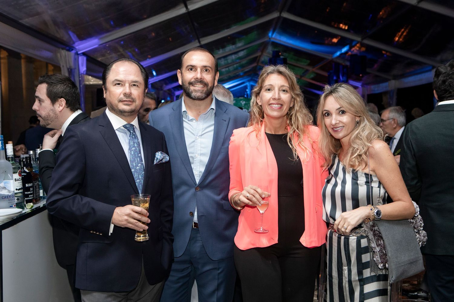 People mingling and networking at an evening corporate event with blue ambient lighting in the background.