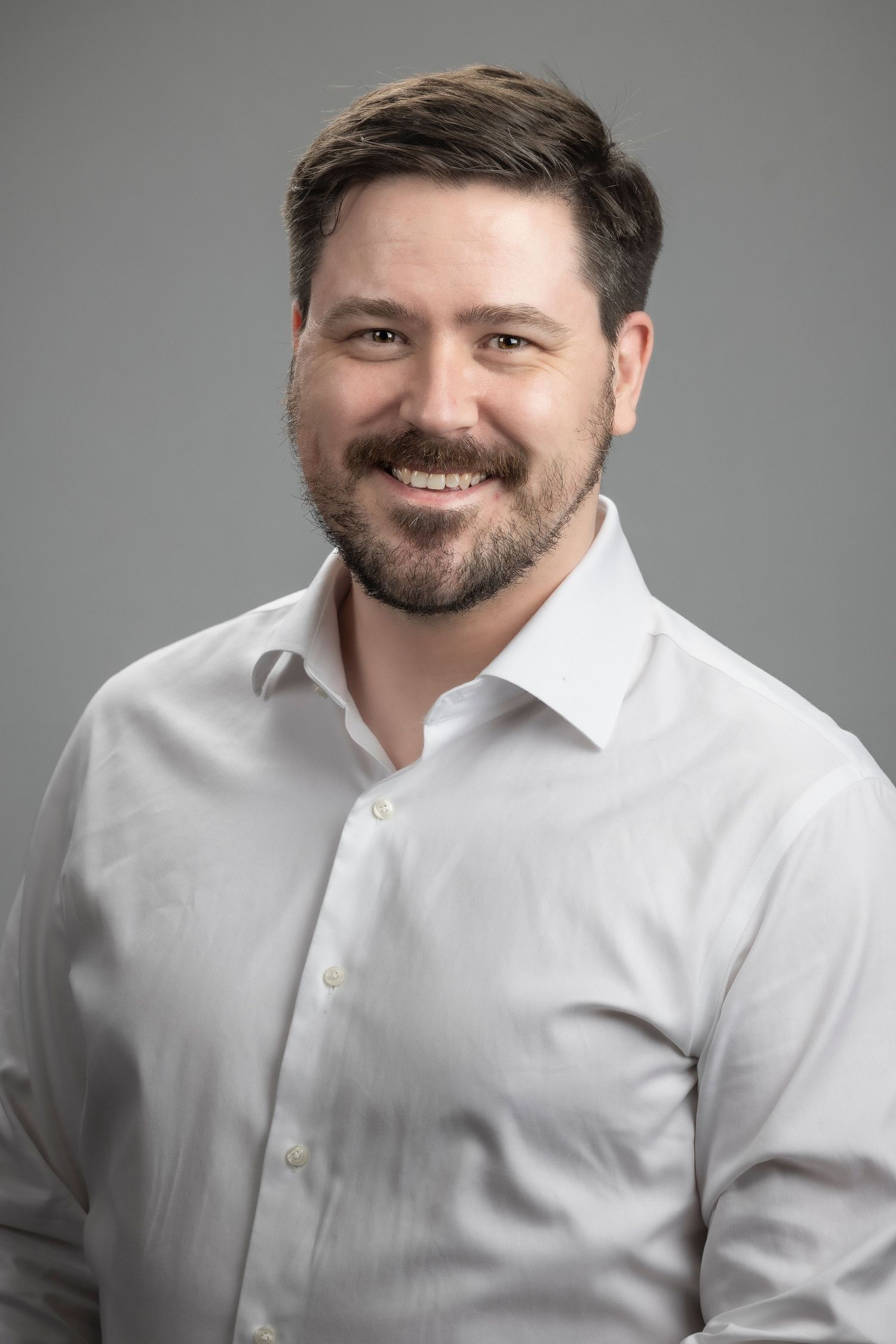 Professional headshot series showing expressive brown-bearded person in white dress shirt against gray background.