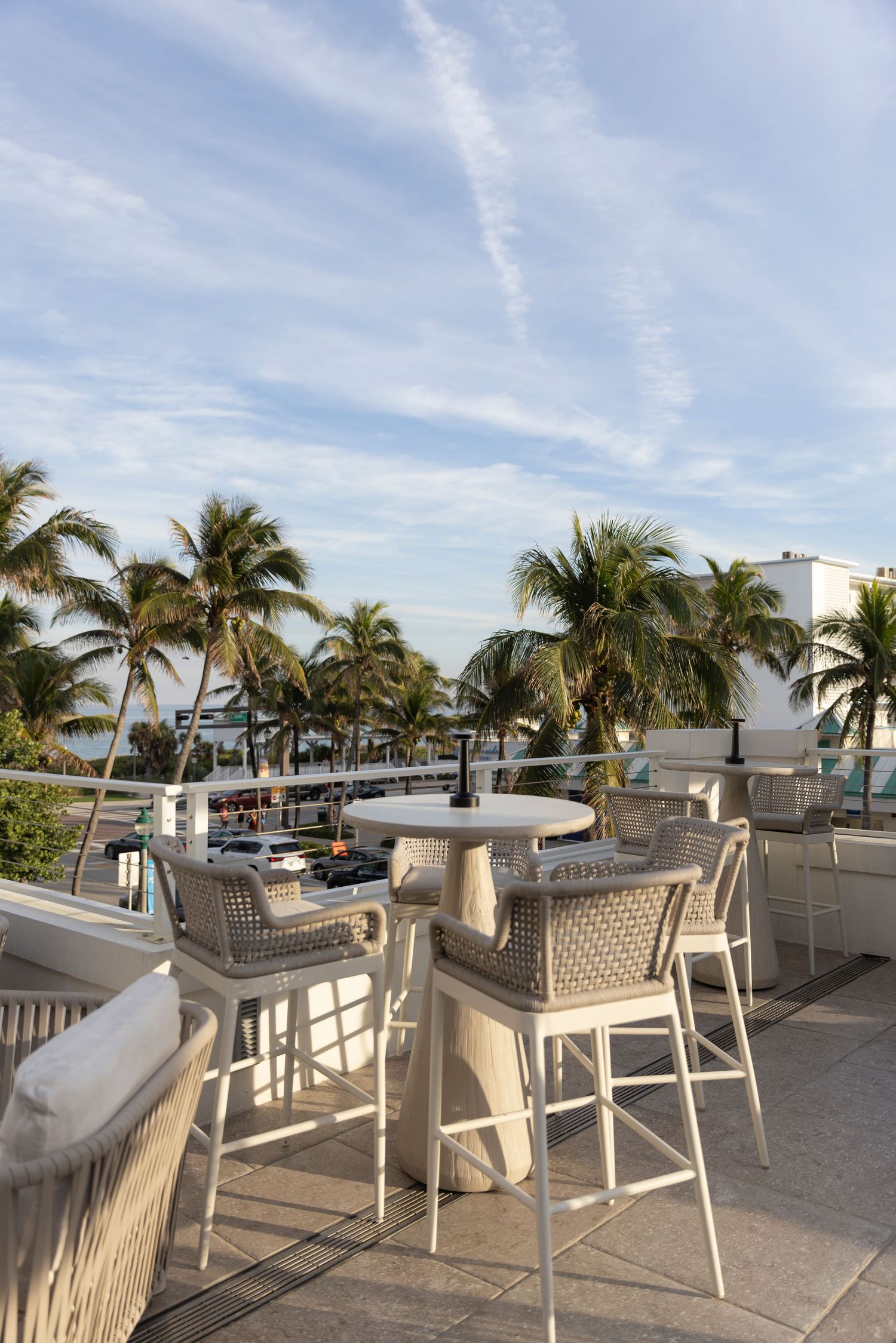 A scenic rooftop restaurant terrace with palm trees, white furniture and ocean views on a sunny day.