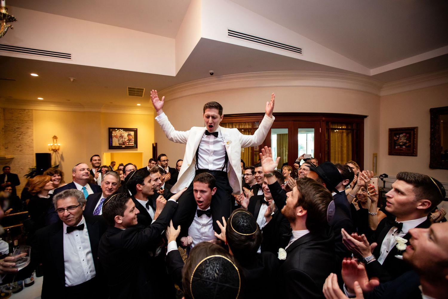 Wedding guests celebrate with raised arms and joyful expressions during a reception party.