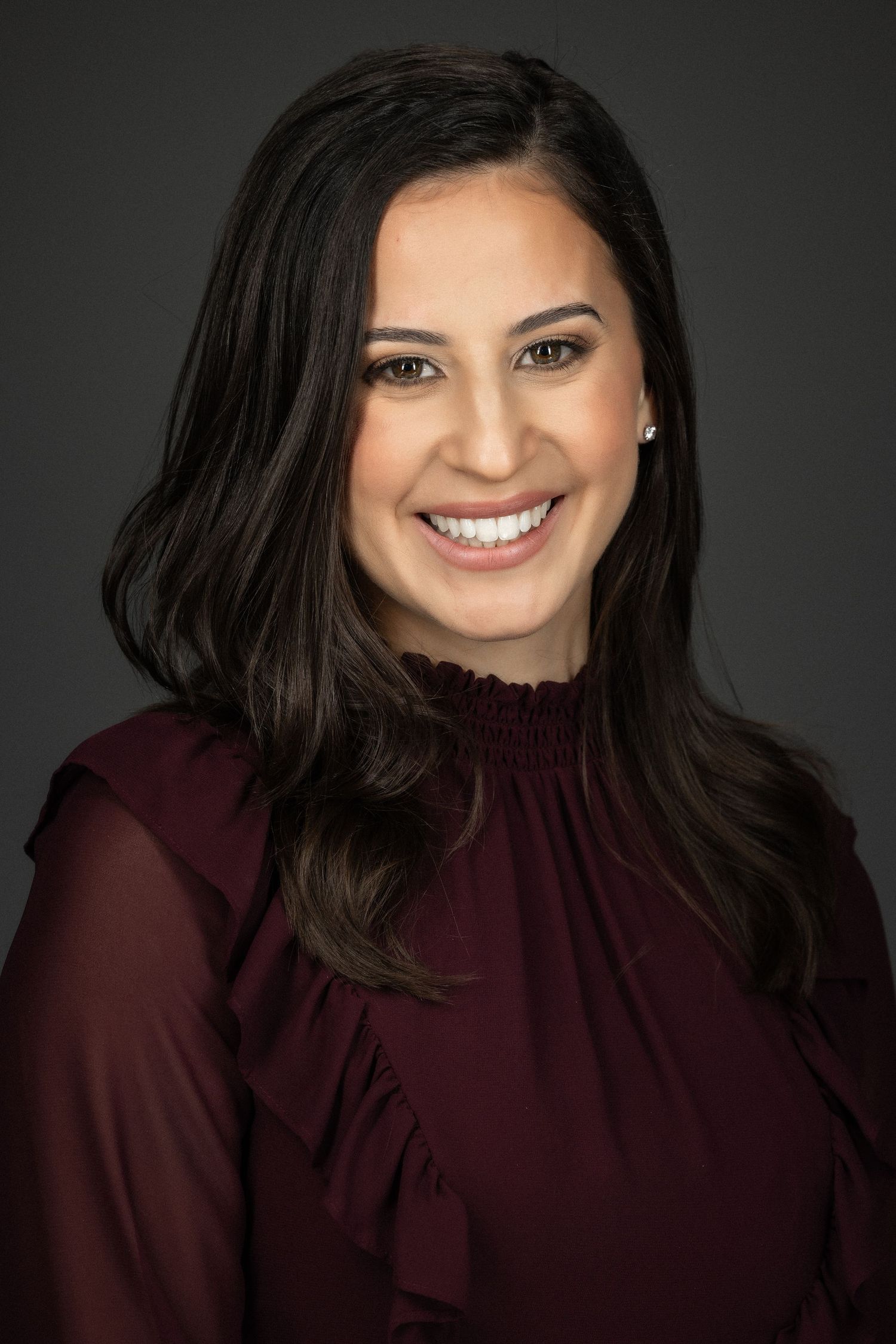 Professional headshot series showing a dark-haired person in burgundy top against gray backdrop with warm expressions.