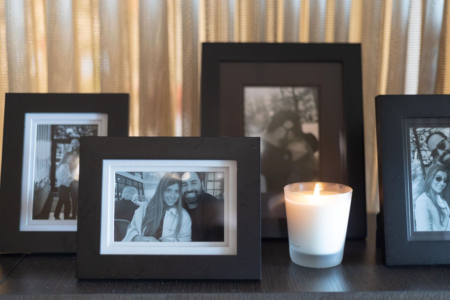 Black and white framed photos displayed on a shelf with a lit white candle in a glass holder.