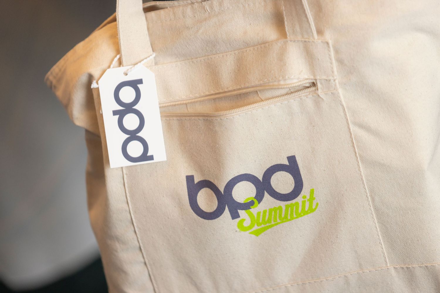 Close-up of a light beige tote bag with 'bpd' company logo and branding details.