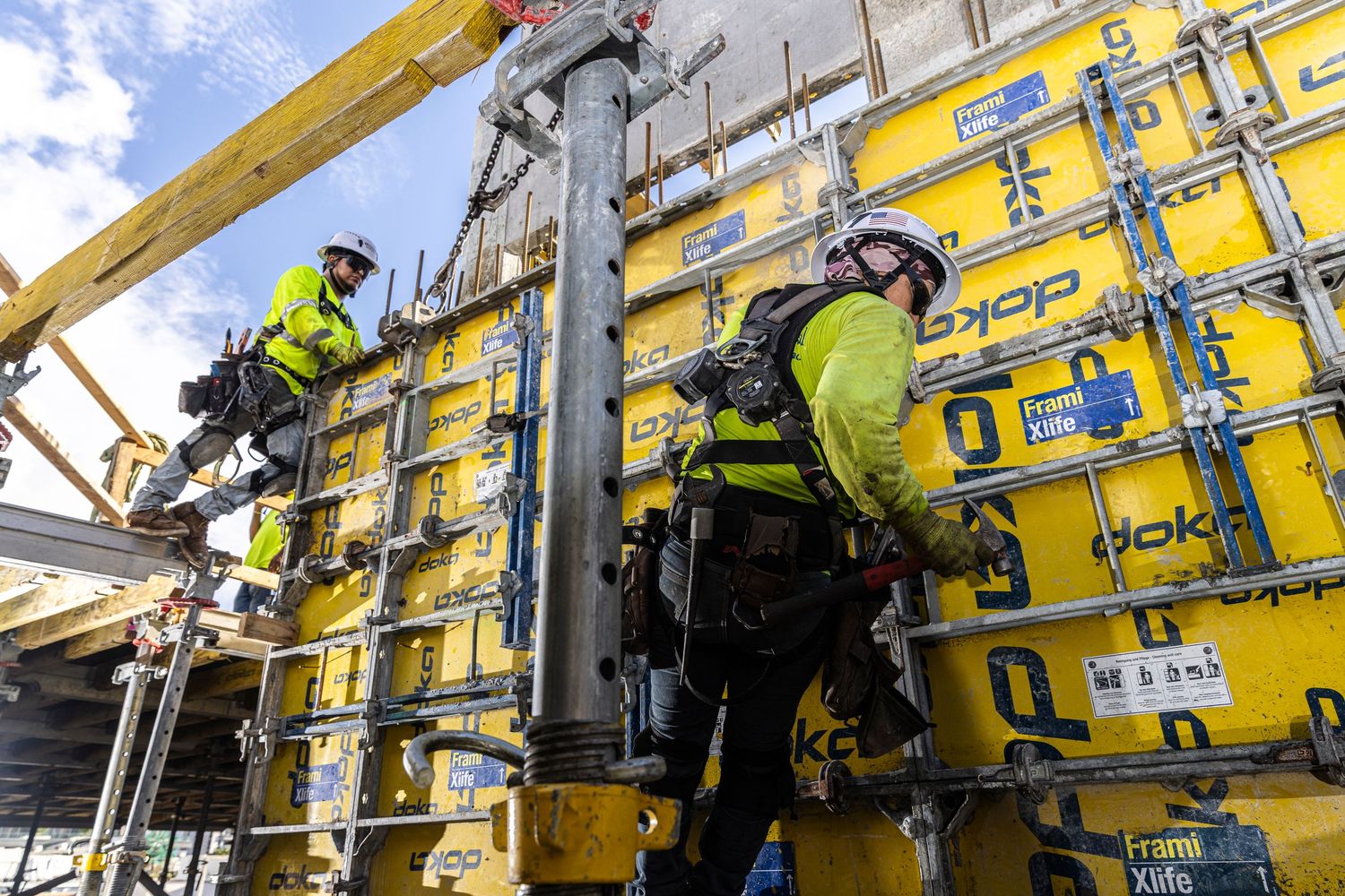 A worker in safety gear performs maintenance on a yellow building facade using climbing ropes and equipment.