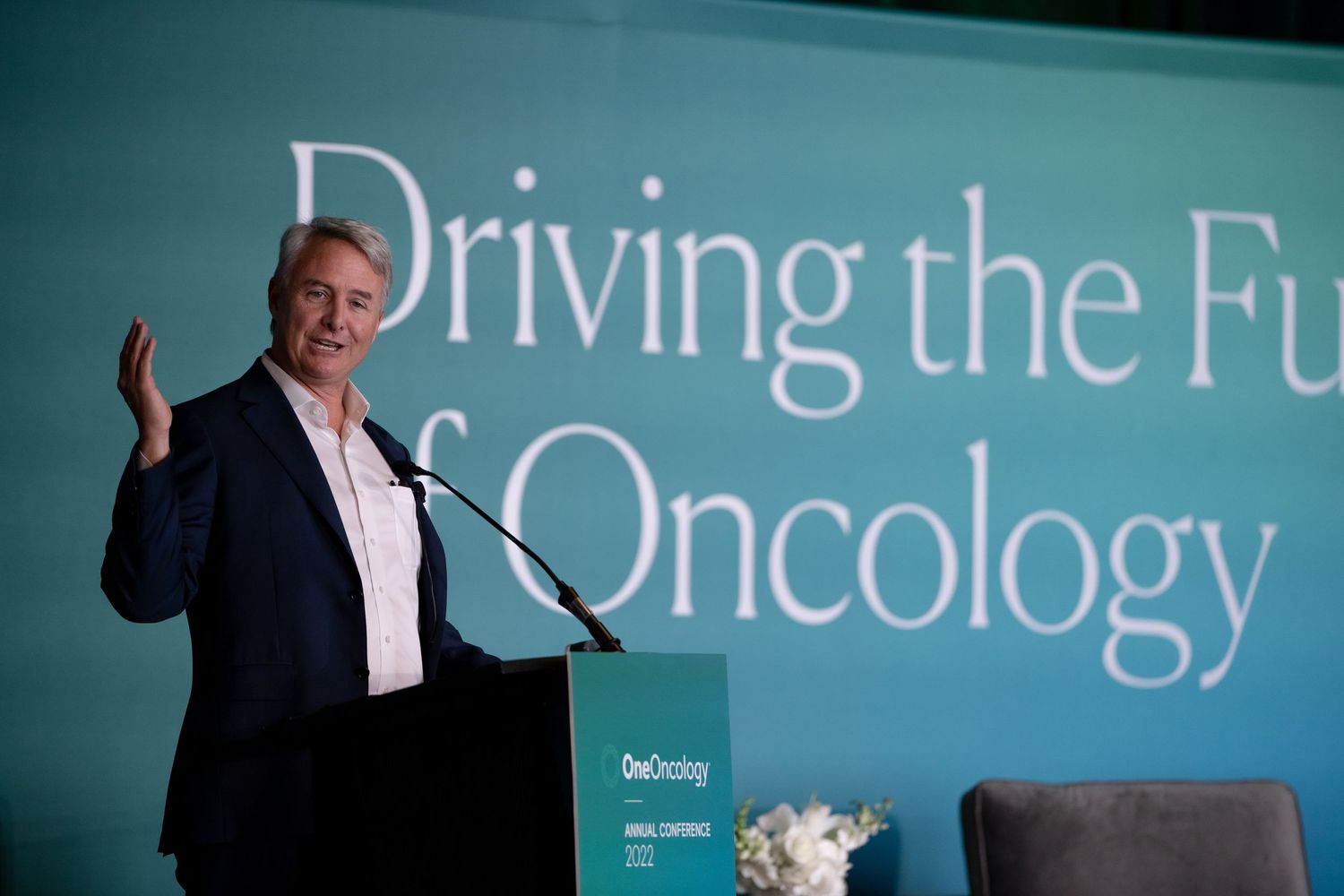 A professional speaker delivers a presentation on oncology at a medical conference with text overlays in blue.