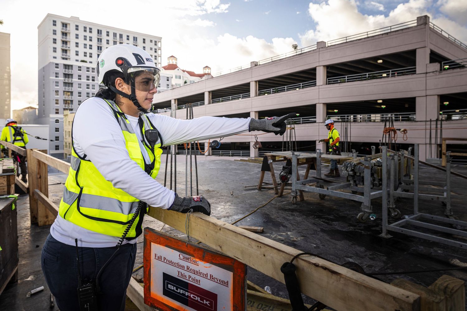 Construction worker in safety vest and hard hat observes progress at multi-level parking structure site.