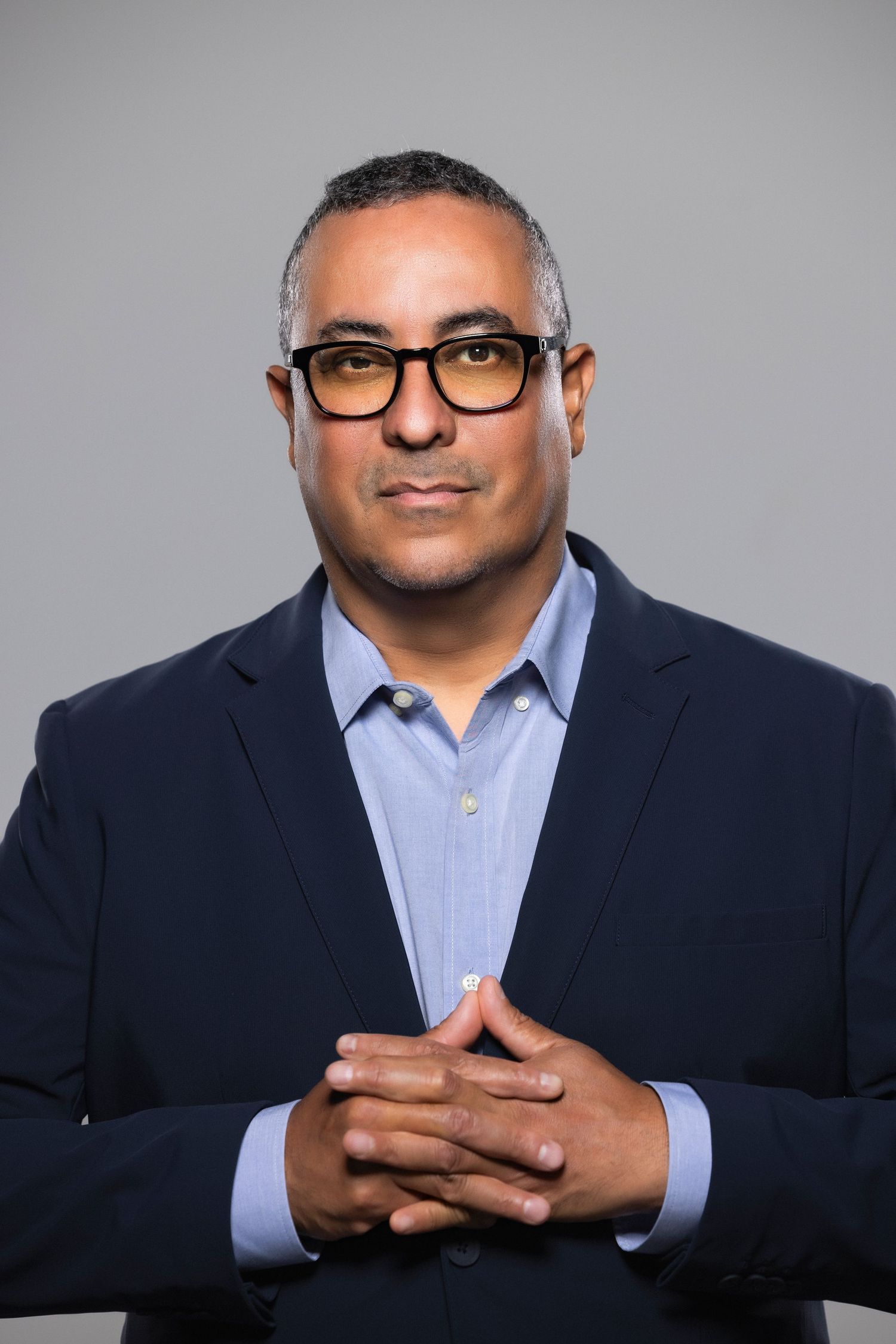 Professional portrait series of person in dark suit and blue shirt against gray background showing different hand gestures.