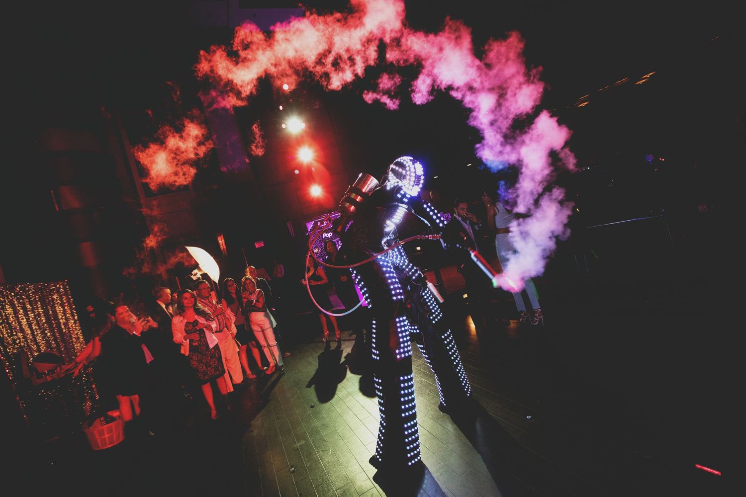 Dramatic performance in smoke with pink and red lighting effects in dark concert or stage setting.